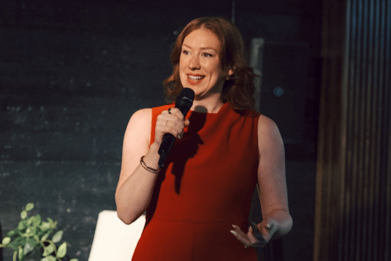 Woman in a red pantsuit speaking into a microphone.