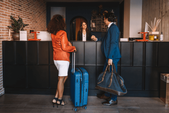 A couple checks in to a hotel where a smiling woman helps them from behind the desk