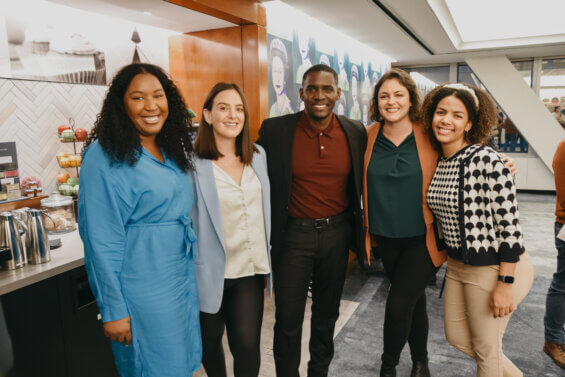 A diverse group of one male and four female DCI staff members stant together and smile at the camera.