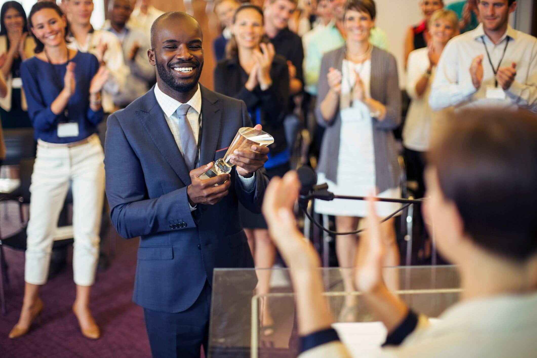 Businessman holds trophy surrounded by crowd applaluding