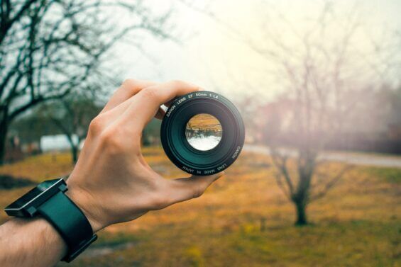 Close-up of man with a modern watch holding a Canon camera lens on a cloudy fall day.