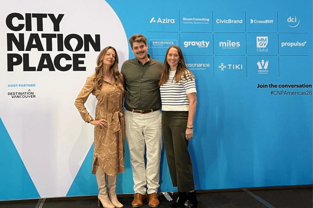 Two women and one man standing in front of a blue step and repeat that reads 