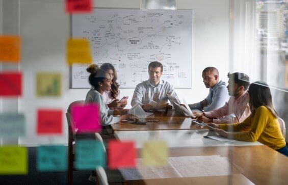 Business people meet around a table with sticky notes in foreground