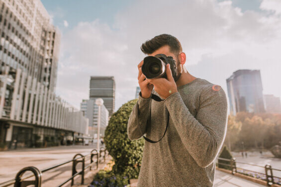 Man in a grey sweater looking through a camera to take a photo