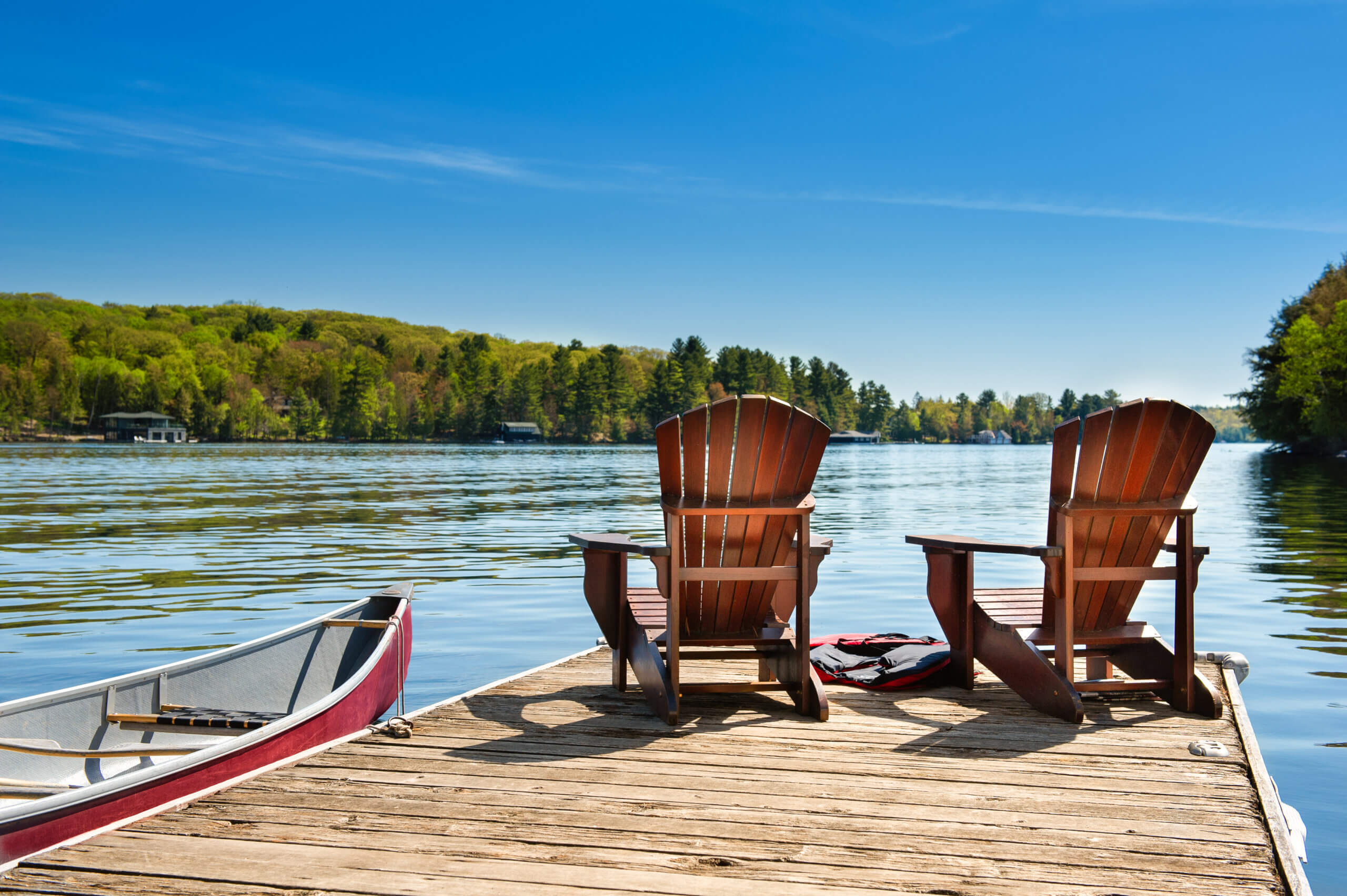 Two Adirondack chairs on a dock on a lake in Canada