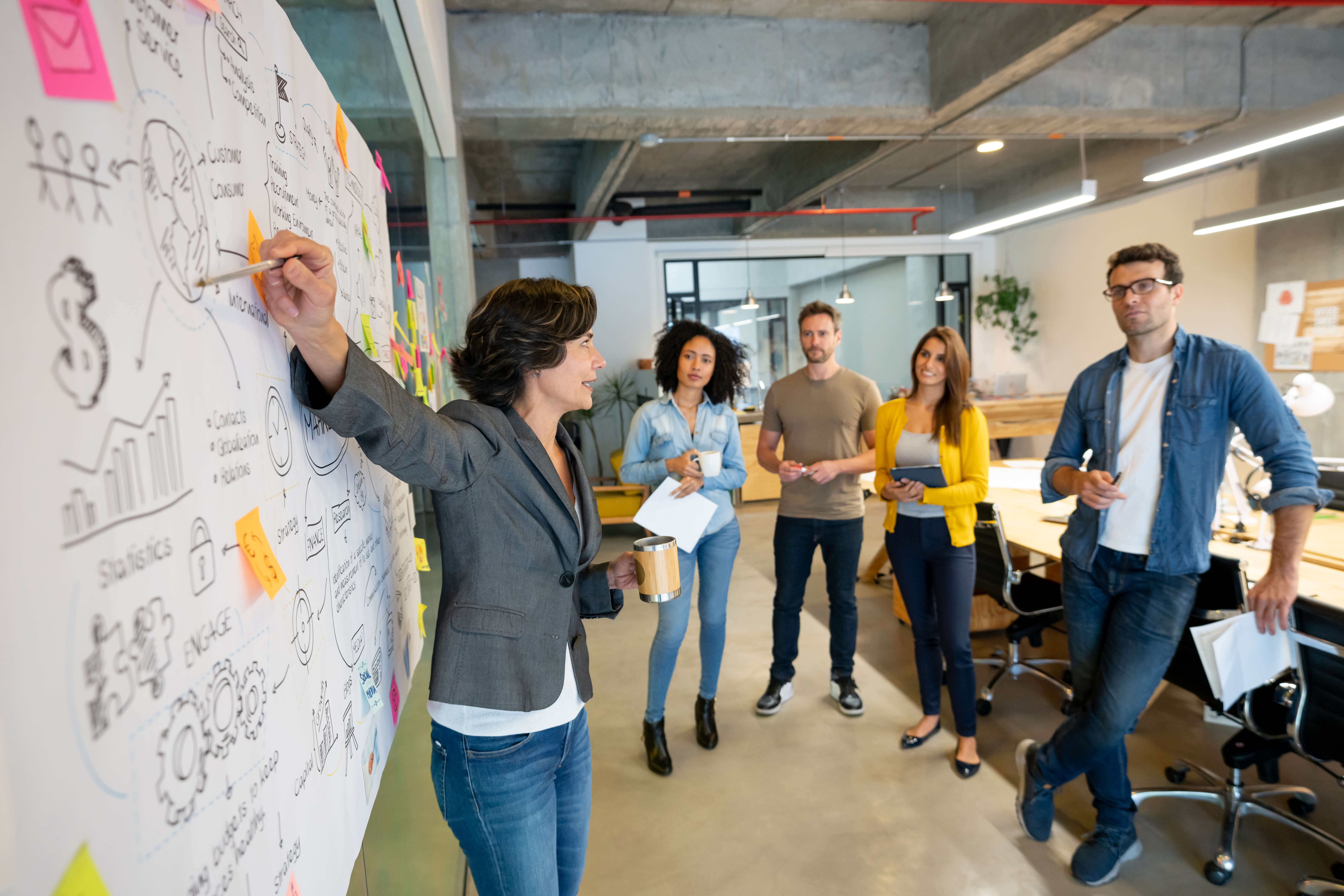 Latin American woman making a business presentation about taglines in a meeting at a creative office and pointing to her team her business plan.