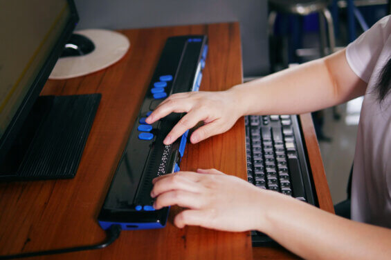 A person with blindness uses a computer with a braille terminal. Using alt tags is important for diversity in digital marketing efforts.