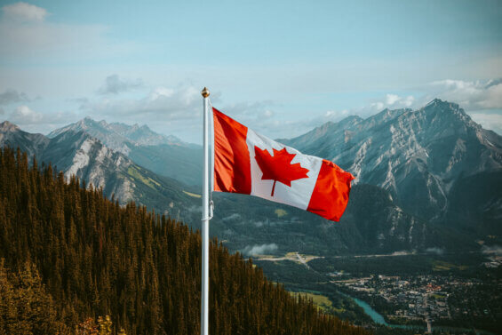 Canada flag flying in front of a mountain landscape.