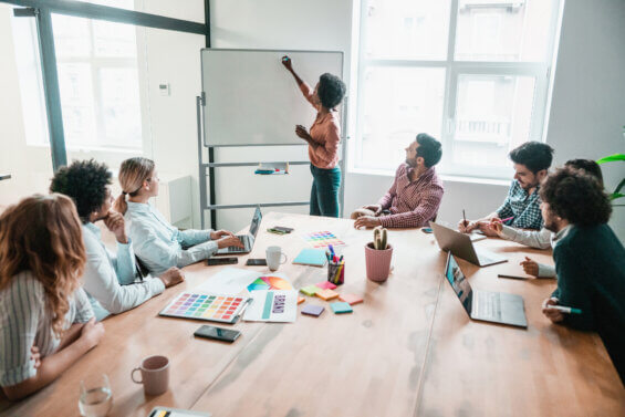 Woman drawing on a white board in a meeting room full of coworkers