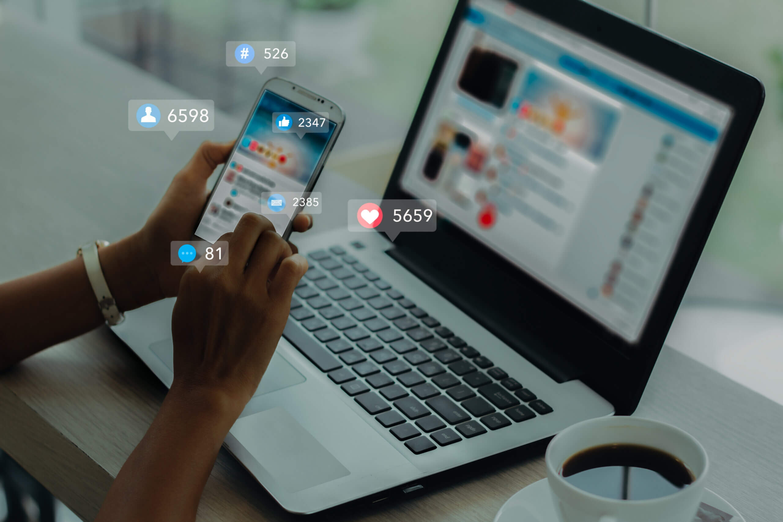 Hand holding a phone in front of an open computer with LinkedIn reaction emojis floating in the air around it.