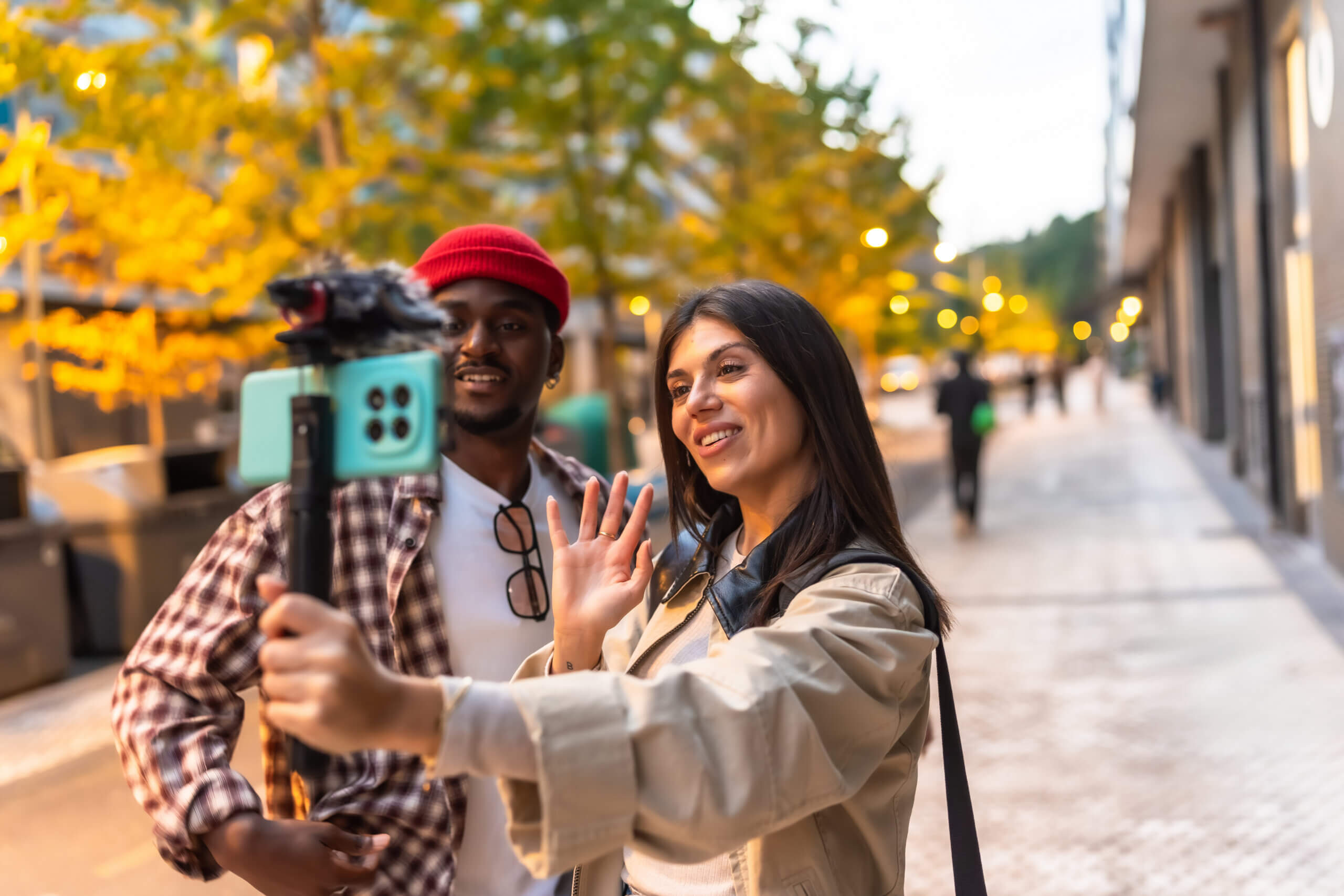 Two young adult friends creating social media content outdoors, filming a live video with a smartphone on a gimbal stabilizer while walking along a urban sidewalk