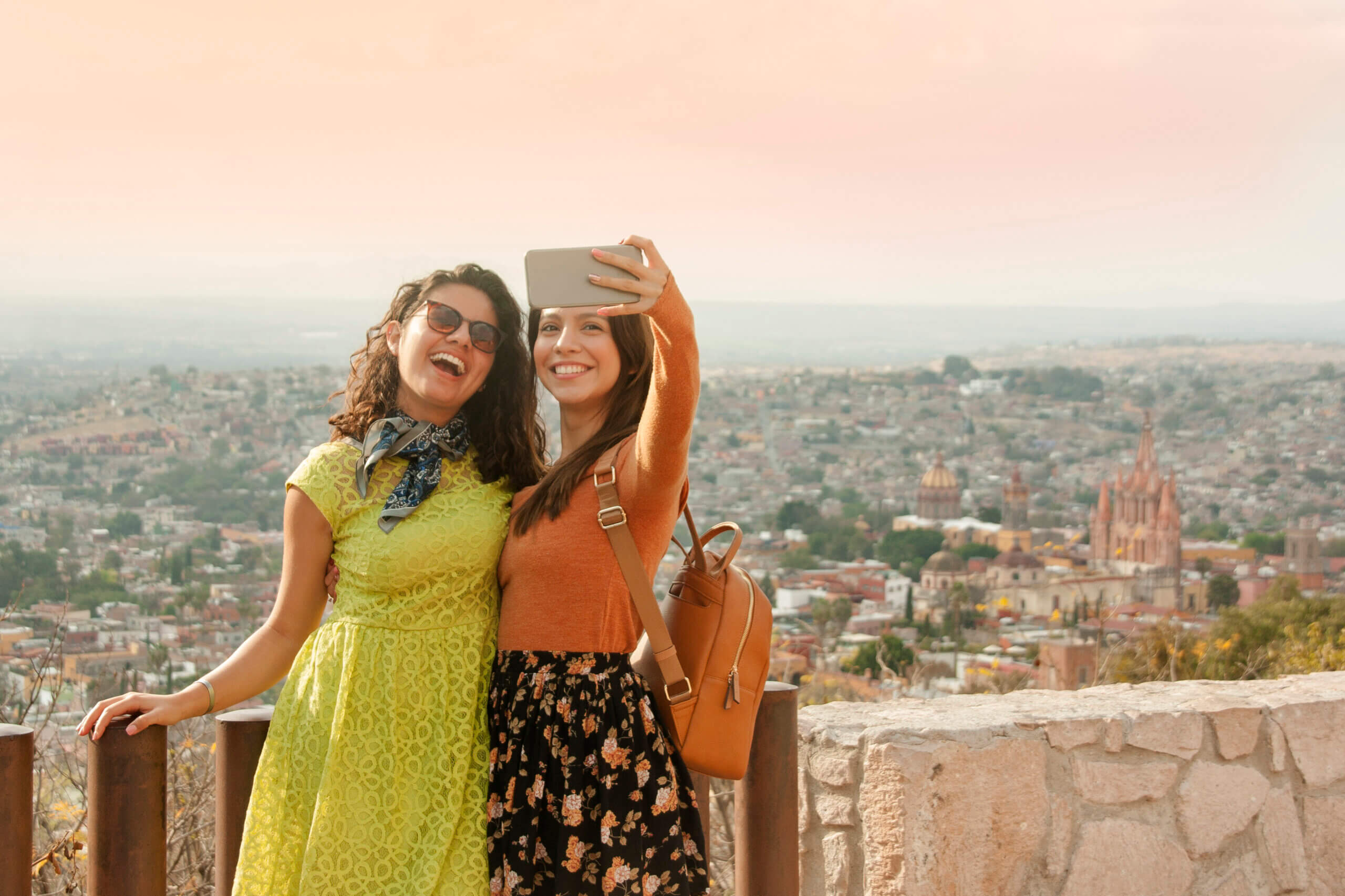 Two Latina women taking a selfie overlooking a city.