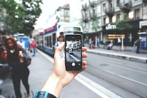 A hand holds up a phone to take a picture of an urban streetscape